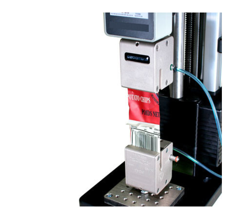 Twee G1046-grepen getoond in een typische 180°-verwijderingstest van een verzegelde verpakkingsstrip, gebruikt in combinatie met een digitale krachtmeter en testbank.